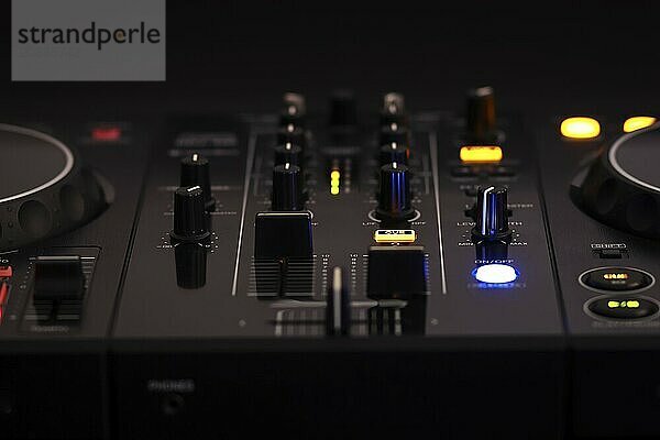 A black DJ mixer with various buttons and knobs  illuminated against a dark background  creating a professional and rhythmic ambiance  mixer dj audio