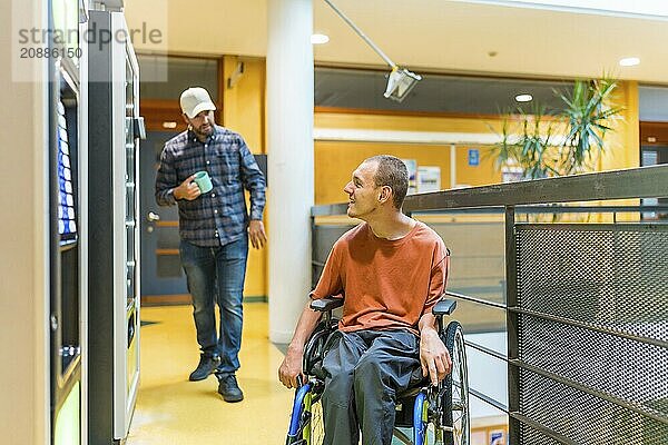 Coworkers walking into vending machines in a work break. One of them are a man with disability sitting on wheelchair