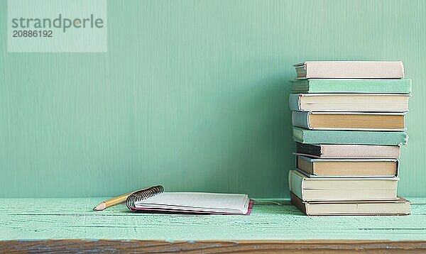 Stack of books on a wooden desk with a pastel mint green background AI generated