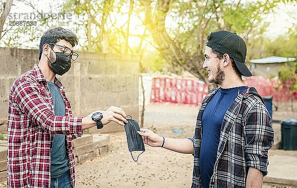 Concept of a person giving a surgical mask  Two young people giving each other a surgical mask  Side view of young man giving a surgical mask to another person outdoor