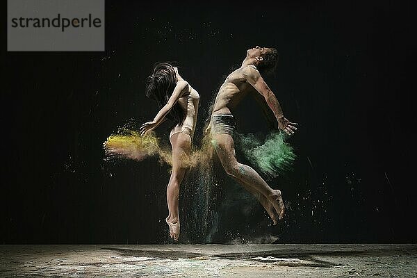 Young man and woman posing emotionally in jump face to face to each other in cloud of yeloow and green dust studio shot