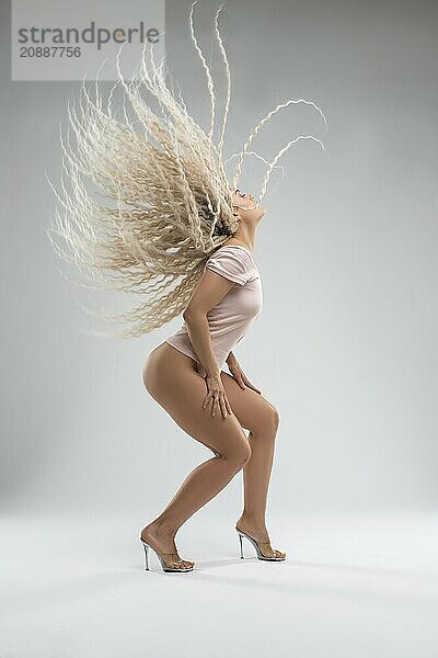 Side view full body of sensual young fit female with long blond curly hair in t shirt and high heeled sandals shaking head while dancing