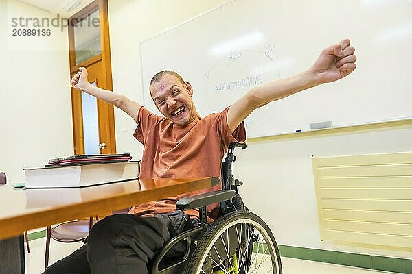 Man with disability proud of himself in the university celebrating raising arms sitting on wheelchair