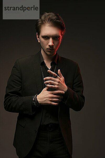 Serious young man in elegant suit touching chin and looking at camera  evil concept