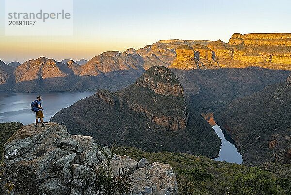 Young man standing on rocks and enjoying the view  sunset at Blyde River Canyon with Three Rondawels peak  view of canyon with Blyde River and table mountains in the evening light  canyon landscape  Panorama Route  Mpumalanga  South Africa  Africa