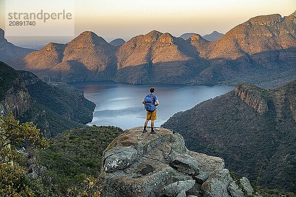 Young man standing on rocks and enjoying the view  Sunset at Blyde River Canyon View of canyon with Blyde River and table mountains in the evening light  Canyon landscape  Panorama Route  Mpumalanga  South Africa  Africa