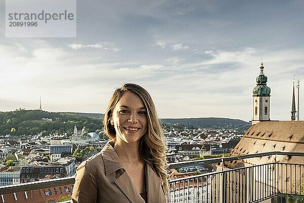 A woman smiles on a balcony above a cityscape in the evening light with a church tower in the background  ai generated  KI generated  AI generated