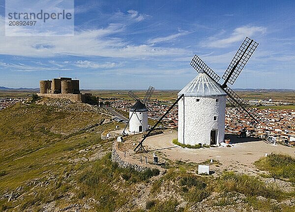 Windmills on a hill with a medieval castle in the background towering over a nearby village with a cloudy sky  aerial view  Consuegra  Toledo  Castilla-La Mancha  Spain  Europe