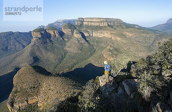 Tourist standing on a rock and enjoying the view of the canyon  Blyde River Canyon with Three Rondawels peak  View of canyon with Blyde River and Table Mountains  Canyon landscape in the evening light  Three Rondavels Viewpoint  Panorama Route  Mpumalanga  South Africa  Africa