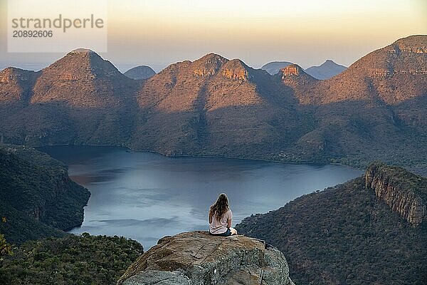 Young woman sitting on a rock  enjoying the view  sunset at Blyde River Canyon  view of canyon with Blyde River and table mountains in the evening light  canyon landscape  Panorama Route  Mpumalanga  South Africa  Africa