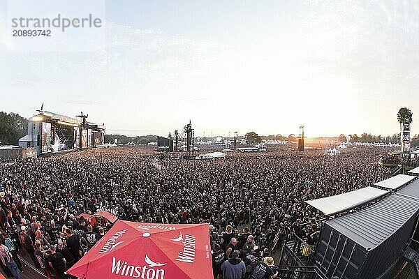 Overview of the crowd with the setting sun and the two main stages Faster and Harder at the Wacken Open Air in Wacken. The traditional metal festival takes place from 31 July to 3 August 2024. Note: the photo was taken with a fisheye lens