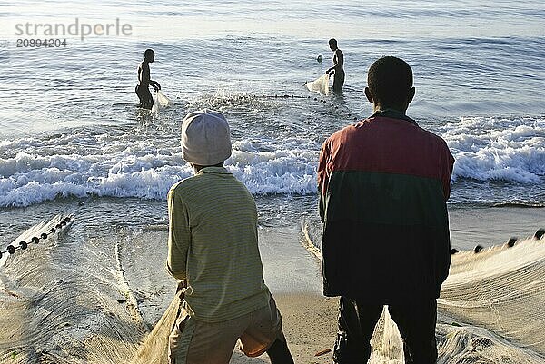 Boys are pulling a fishing net out of the water. Two fishermen are helping them. At Toamasina Madagascar