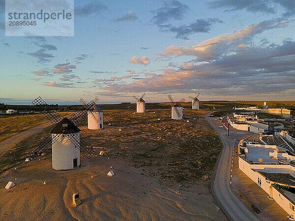 Landscape at sunset with windmills and a road leading to an illuminated village  aerial view  windmills  Campo de Criptana  Ciudad Real province  Castilla-La Mancha  Route of Don Quixote  Spain  Europe