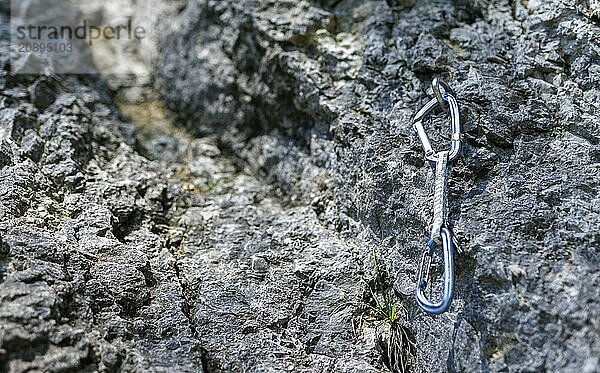 A carabiner hangs from a hook on a rock face. Climbers use the so-called quickdraws to secure themselves with the rope on a climbing route. Taken in Morsbach  09.07.2024