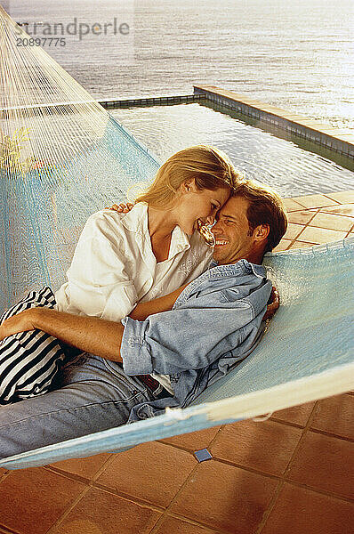 Young romantic couple sharing a hammock on waterside terrace.