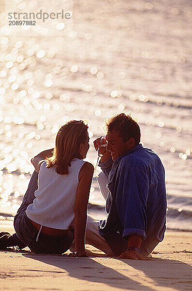 Young man and woman sitting on a beach at sunset.