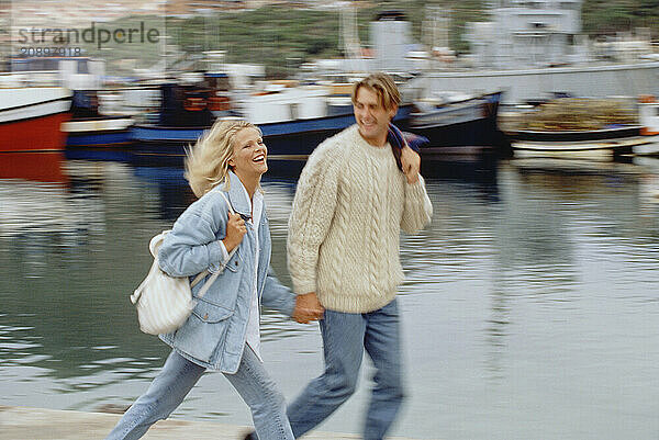 South Africa. Cape Town. Motion impression of young couple walking on quay by boats in harbour.