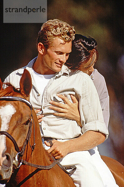 Close up of young couple outdoors riding together on one horse.