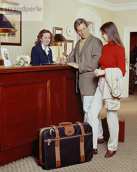 Young couple checking in at hotel reception desk.