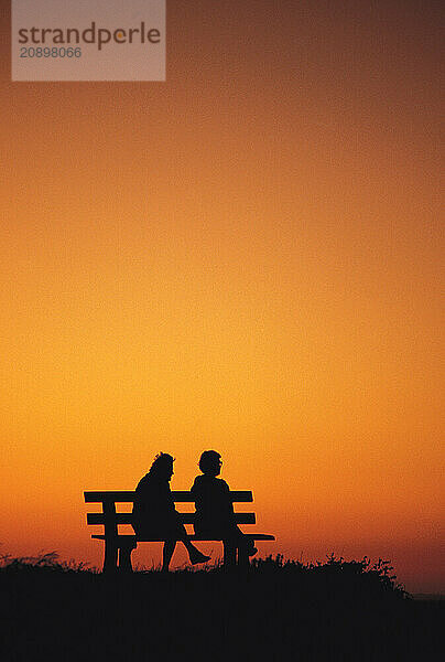 Two old women sitting on park bench at sunset.