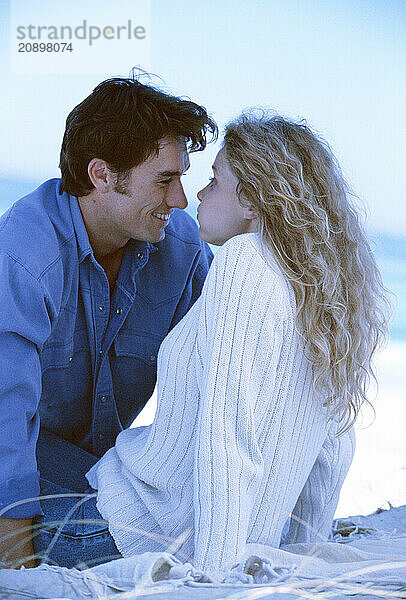 Young couple in warm clothes sitting on the beach.