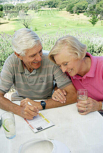 Close up of retired couple sitting outdoors at golf club. Checking the scorecard.