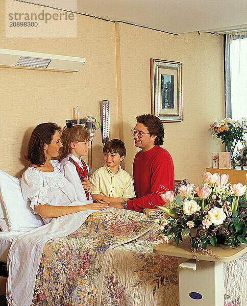 Hospital visit. Man & children visiting woman patient in bed.