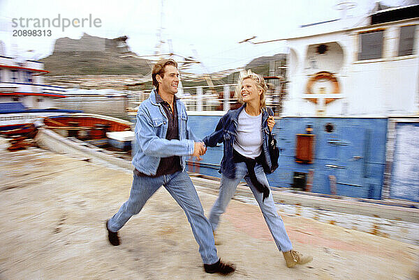 South Africa. Cape Town. Motion impression of young couple walking on quay by boats in harbour.