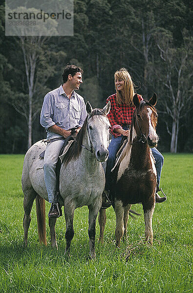 Young couple outdoors riding horses.