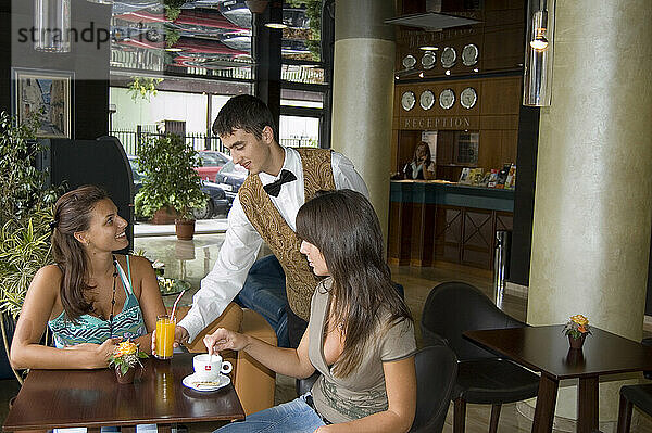 Bulgaria. Sofia. Café. Lobby bar of Great Western Hotel. Waiter serving two young women.