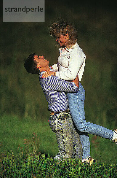 Young romantic couple outdoors in countryside. Man lifting woman.