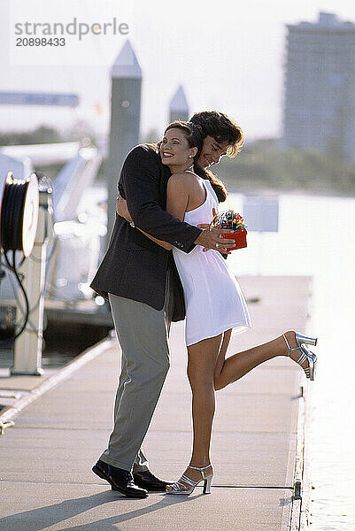 Australia. Queensland. Gold Coast. Young couple embracing on marina pontoon.