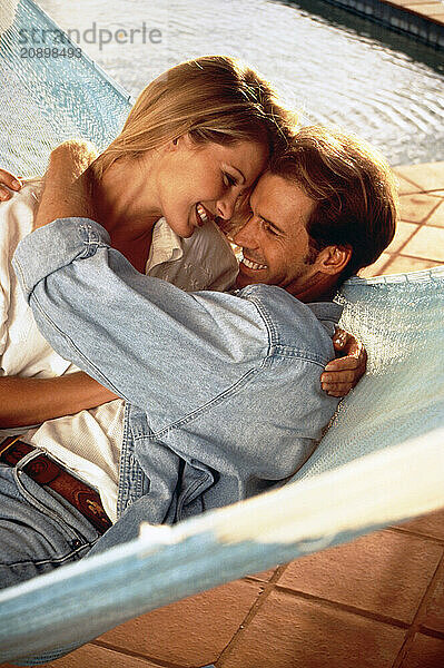 Young romantic couple sharing a hammock on poolside terrace.