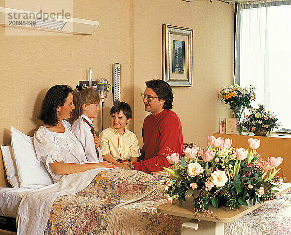 Hospital visit. Man & children visiting woman patient in bed.