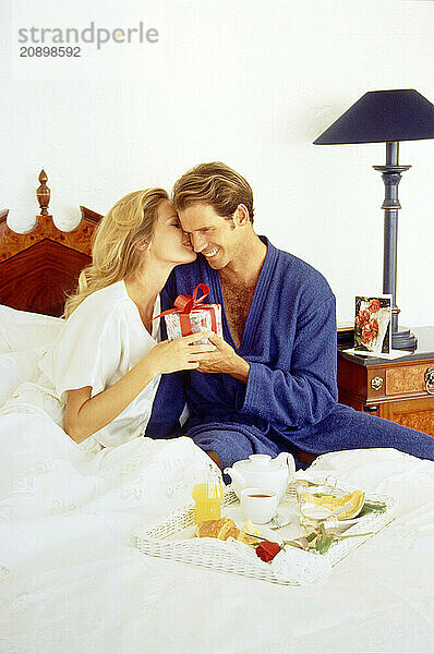 Young couple in bed with special occasion gift and breakfast tray.