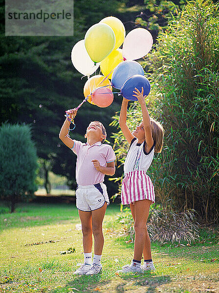 Children. Boy and girl playing with bunch of balloons outdoors in park.