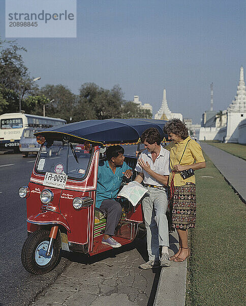 Thailand. Bangkok. Tourists speaking with tuk-tuk taxi driver at the roadside.