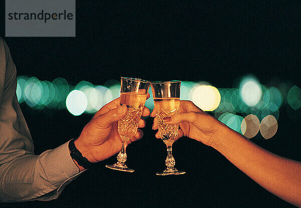 Lifestyle. Man & woman. Celebrating. Close up of hands chinking Champagne glasses.