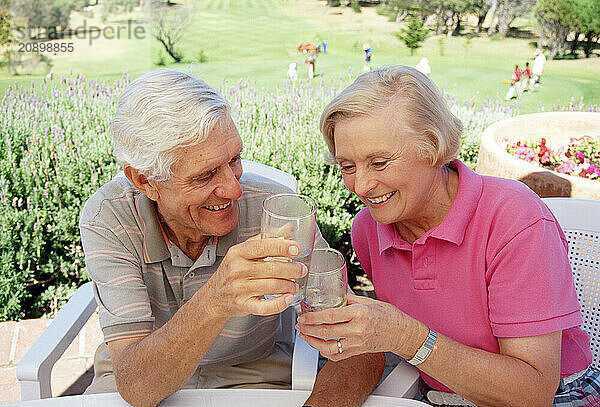 Old couple relaxing with drinks on golf club terrace.