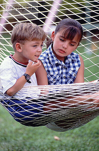 Children. Boy & girl outdoors in hammock.