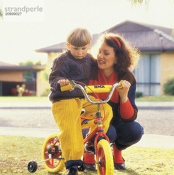 Mother & four-year-old son with bicycle in suburban street.