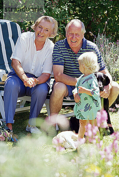 Grandparents with little girl outdoors in garden.