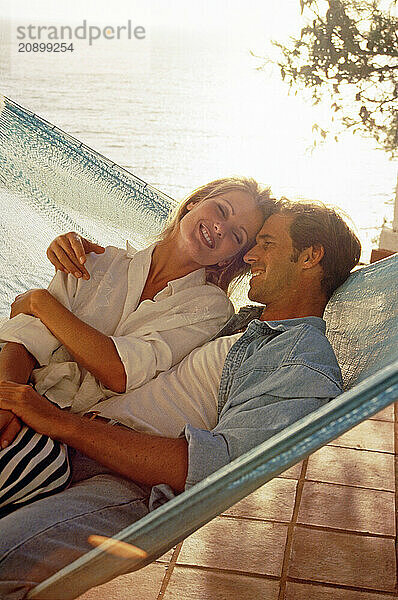 Young romantic couple sharing a hammock on waterside terrace.