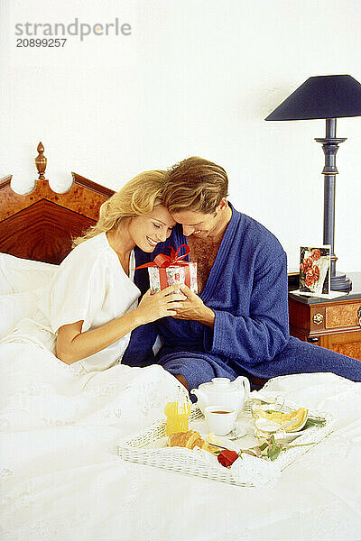 Young couple in bed with special occasion gift and breakfast tray.