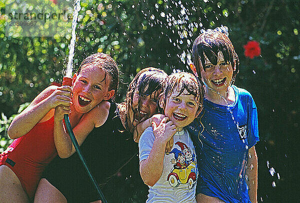 Australia. Group of children with water hose playing outdoors in garden.