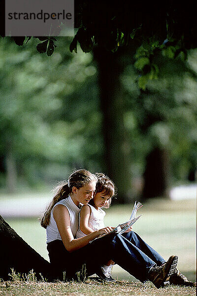 Teenage woman & little girl sitting together in an urban park.