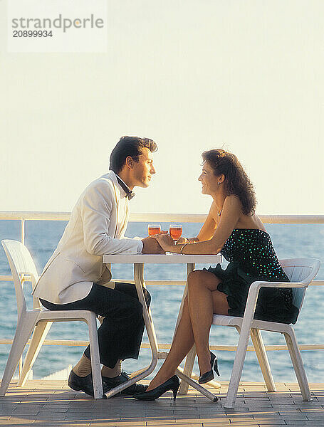 Spain. Marbella. Side view of young couple with wine glasses  sitting on terrace of waterside bar.