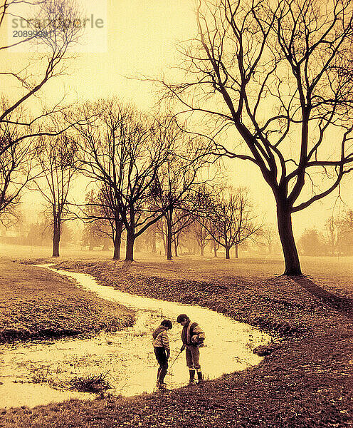 Children. Two boys playing by a stream in misty park.