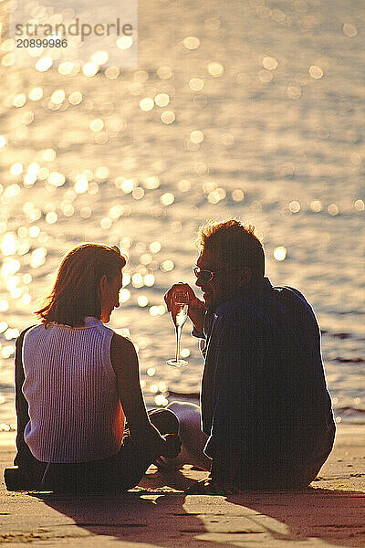 Young man and woman sitting on a beach at sunset.