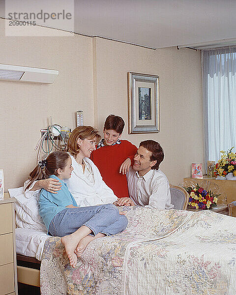 Hospital visit. Man & children visiting woman patient in bed.